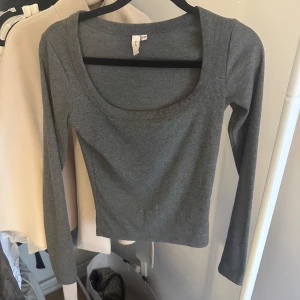 Grå ribbad topp från Nelly - Snygg grå långärmad topp från Nelly med ribbad struktur och djup rundad urringning. Modellen är figurnära och passar perfekt till jeans eller kjol. Enkel och stilren design som är lätt att matcha.
