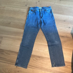 Wrangler Texas blå jeans W31 L32 - Klassiska blå jeans från Wrangler, modell Texas. Raka ben och normal passform med fem fickor och snygga kontrastsömmar. Tillverkade i slitstarkt bomullsjeans. Perfekta för dig som gillar en tidlös och avslappnad look. Jag vill även nämna att det finns ett litet hål längst ner vid benen på byxorna.