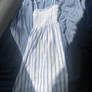 Randig sommarklänning  - Supersöt långklänning från H&M i blått och vitt med smockad överdel och tunna axelband. Klänningen har ett randigt mönster och är gjord i luftig bomull, perfekt för varma dagar. Säljer då jag aldrig anväde den efter att ha köpt den i fjol.