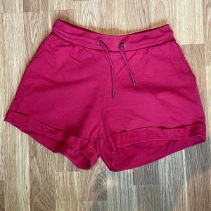 Röd shorts  - Snygga mörkrosa shorts med uppvikta benslut och bekväm resår i midjan. De har snörning framtill och två sidofickor. Perfekta för varma dagar och chill häng. Materialet känns mjukt och skönt mot huden.