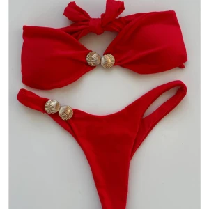Röd bandeaubikini med snäckdetaljer designbysi - Snygg röd bandeau bikini som knyts i ryggen och dekorativa guldfärgade snäckor både på toppen och underdelen. Helt oanvänd!🥰(säljer här pga frakt och retur kostar mer)