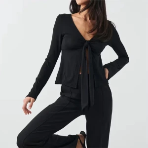 Svart långärmad knytblus - Svart långärmad blus med djup v-ringning och snygg knytning framtill. Modellen är croppad och har en flowy passform som ger en cool och trendig look. Perfekt att styla med höga byxor för en stilren outfit.
