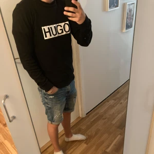 Svart långärmad tröja från HUGO - Svart långärmad tröja från HUGO med stor vit logga framtill. Klassisk rund halsringning och normal passform. Perfekt för dig som gillar stilrena och enkla plagg med tydlig branding. Skön att bära och lätt att matcha med jeans eller shorts.