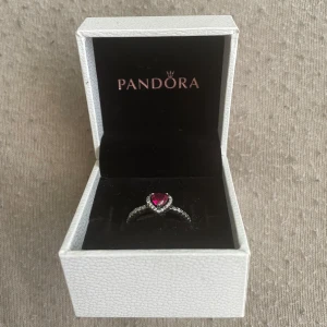 Pandora silverring med hjärta - Superfin silverring från Pandora med ett rött hjärta i mitten, omgiven av små gnistrande stenar. Äkta 925 silver och all tillbehör tillkommer med ringen. Helt ny och aldrig använd innan.