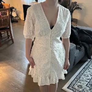Midsommarklänning❤️ - Säljer en söt vit kortklänning med broderad spets och volangkant nertill. Klänningen har v-ringning, korta puffärmar och knappar framtill och korsett liknande fram. Perfekt till midsommar❤️Helt ny med lappar❤️ Köpt 699kr