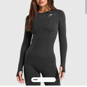  långärmad compression shirt från Gymshark - Svart seamless långärmad topp från Gymshark med tight passform och diskret strukturmönster. Toppen har tumhål vid ärmsluten och en liten vit logga på bröstet. Perfekt för träning och ger en snygg, sportig look. Använd några enstaka gånger och är i mycket fint skick.