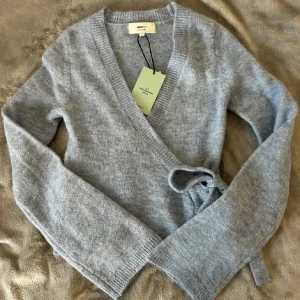 Ljusblå omlottkofta från Gina Tricot - Superfin ljusblå omlottkofta från Gina Tricot i mjuk ullblandning. Koftan har långa ärmar, ribbade muddar och knytband i sidan för en snygg passform. Perfekt att slänga på sig när det är lite kyligt ute.