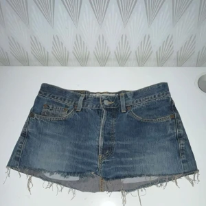 Blå jeansshorts med fransig kant - Snygga blå jeansshorts med rå, fransig kant och klassisk femficksdesign. Shortsen har bälteshällor och knappgylf. Perfekta för varma dagar när du vill ha en avslappnad och cool stil.