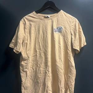 Beige t-shirt från Moncler  - Snygg beige t-shirt från Moncler i storlek XXL. T-shirten skulle säga L har klassisk rund hals, korta ärmar och en broderad Moncler-logga på bröstet. Tillverkad i mjuk bomull som känns skön mot huden. Perfekt för dig som gillar stilrena och exklusiva plagg.