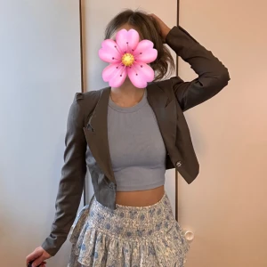 Grå croppad kavaj med knapp - Snygg brun croppad kavaj med markerade axlar och en knapp framtill. Jackan har långa ärmar och breda slag, vilket ger en trendig och stilren look. Perfekt att styla över en topp eller klänning för en cool vibe.