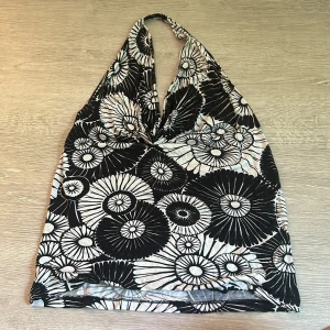 Svartvit blommig halterneck topp vintage H&M - Supersnygg halterneck topp från vintage H&M i svartvitt blommigt mönster. Toppen har djup v-ringning och är ärmlös, perfekt för varma dagar eller när du vill sticka ut lite extra. Mjuk och stretchig i materialet, lätt att styla med jeans eller kjol.