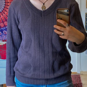 Mörklila/brun stickad v-ringad tröja - Mysig mörklila stickad tröja med v-ringning med mönster i strukturen. Tröjan har långa ärmar och ribbade muddar vid ärmslut och nederkant. Väldigt mjukt material, känns skön mot huden. Inga defekter