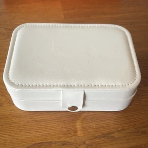 Vit smyckesväska - Snygg och stilren smyckesväska i vit skinnimitation med praktiska fack och hållare för ringar, örhängen och halsband. Perfekt att ha på resan eller hemma på hyllan. Stängs med tryckknapp och har en mjuk insida som skyddar dina smycken.