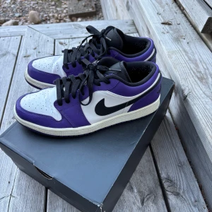Nike Air Jordan 1 Low Court Purple - Säljer ett par Nike Air Jordan 1 Low i färgen Court Purple. Skorna har en snygg kombination av vitt, svart och lila skinn, klassisk svart swoosh och svarta snören. Ikonisk Air Jordan-logga broderad på hälen. Perfekta för dig som vill sticka ut med stil.                                                                       Använda max fyra eller fem gånger.