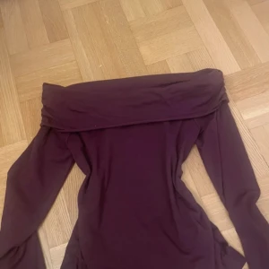 Vinröd offshoulder topp - Säljer en vinröd offshoulder topp med lång ärm och tight passform. Toppen har en bred, vikt kant över axlarna som ger en snygg och trendig look. Perfekt att styla med jeans eller kjol för en cool vibe.