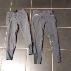 2 Grå ridbyxor med silikongrepp stl 150/ 160 - Två par grå ridbyxor med silikongrepp på insidan av benen och bak. Ena paret har snygga broderade detaljer på bakfickorna och dragkedja, medan det andra har en mer stilren look. Båda har hög midja och smal passform, perfekta för ridning. Stl 150 cl och ca 160 cl. Köparen betalar frakten.