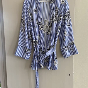 Blus från Gina Tricot, storlek 36 - Snygg blåvit randig blus med svartvita blommor och knytbälte i midjan. Från Gina Tricot, storlek 36. Inga anmärkningar 