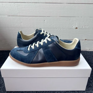 Maison Margiela Gats - Tjena! Säljer mina Maison Margiela Gats i mörkblå mocka och skinn med vita snören och beige innersula. Klassisk retrostil med gummisula och snygga paneler i olika material. Perfekta för dig som gillar stilrena och tidlösa sneakers med en twist. Hör gärna av er! 