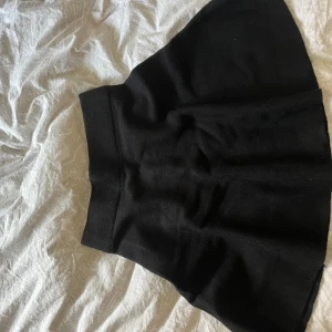 Svart kortkjol från C'est la vie - En svart, enkel och stilren kortkjol från C'est la vie. Kjolen har en lätt utsvängd form och bred midja som ger en snygg siluett. Perfekt att matcha med en stickad tröja eller crop top för en trendig look.