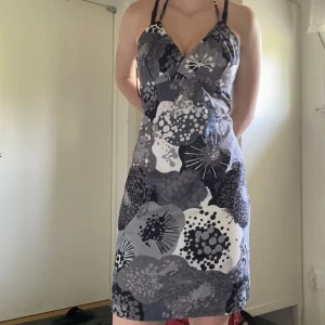 Blommig retro klänning med knytband - Snygg kort klänning med svart, grått och vitt blommönster. V-ringad omlott upptill och smala axelband som knyts i nacken. Strl 40 men passa mindre också skulle jag säga. Köpt secondhand. Pris kan alltid diskuteras. Hör av dig om funderingar uppstår!😇🫶