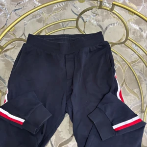 Moncler mjukisbyxor med ränder - Mörkblå mjukisbyxor från Moncler med röda och vita ränder längs sidorna. Byxorna har resår i midjan, muddar vid bensluten och en bakficka med Moncler-logga. Tillverkade i mjuk bomull för maximal komfort och avslappnad stil.