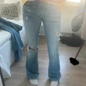 Ljusblå bootcut jeans med slitningar - Säljer ett par ljusblå bootcut jeans med snygga slitningar och hål på knäna. Jeansen har klassisk femficksmodell och normal passform. Perfekta för dig som gillar en avslappnad och trendig look.