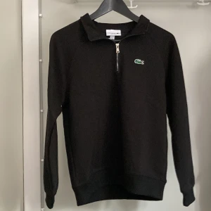 Svart half zip tröja från Lacoste - Svart långärmad tröja från Lacoste med klassisk krokodillogga på bröstet. Tröjan har en snygg half zip-dragkedja vid halsen och är tillverkad av ekologisk bomull och återvunnen polyester. Regular fit med ribbade muddar för en clean look. Nypris 1349kr. Storlek M men känns mer som S. 
