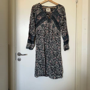 Blommig kortklänning från Star - Supersöt kortklänning från Fira med blommigt mönster i mörkblått, rosa och beige. Klänningen har v-ringning med knyt och långa ärmar. Perfekt för dig som gillar boho-vibe och vill ha något luftigt och bekvämt. Storlek S. Mycket fint skick, jag hittar inga synliga anmärkningar eller defekter.  