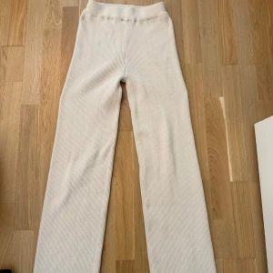 Beiga ribbade mjukisbyxor  - Superbekväma ribbade mjukisbyxor från SHEIN i beige. Byxorna har hög midja och raka, lite vidare ben. Perfekta för chill dagar eller när du vill ha en avslappnad look. Mjukt material som känns skönt mot huden. Storlek S