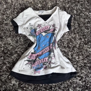 Vit och svart t-shirt med tryck X-Mail - Cool t-shirt från X-Mail i vitt med svarta detaljer och färgglatt tryck framtill med stjärnor, banderoller och rosor. V-ringad hals och korta ärmar. Materialet är mjuk bomull, perfekt för en avslappnad streetstil.