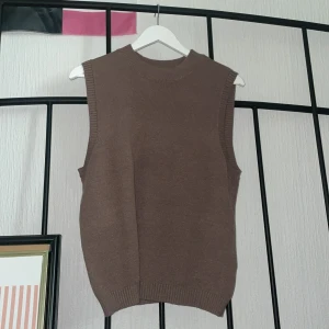 Brun stickad väst från Isolde - En brun stickad väst från Isolde med ribbade kanter vid ärmhål, hals och nederkant. Modellen är ärmlös och har en klassisk, rak passform. Perfekt att styla över en skjorta eller t-shirt för en chill och trendig look. Passar mig som har storlek S/M