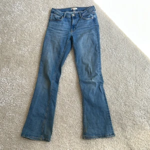 Blå bootcut jeans med fickdetaljer - Snygga blå bootcut jeans med klassisk femficksdesign och coola ficklock med knapp bak. Jeansen har normal passform och är tillverkade i mjukt denimtyg. Perfekta för dig som gillar en avslappnad men trendig look. Säljer då jag tycker de är för highwaist på mig😁. Endas använd ett få tal gånger!!