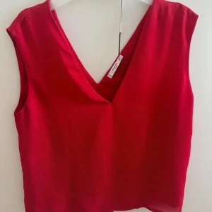 Röd v-ringad linnetopp från Mango - Snygg röd linnetopp från Mango med djup v-ringning och ärmlös design. Perfekt för att skapa en stilren och trendig look. Lätt och luftig känsla, passar till både jeans och kjol