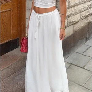 Vit långkjol med snörning - Superfin vit långkjol med flowigt fall och snörning i midjan. Kjolen har en luftig och lätt känsla, perfekt för varma dagar. Passar snyggt till crop tops eller linnen och ger en chill och fräsch vibe. I storlek S aldrig använd, pris lapp kvar 