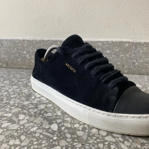 Svarta sneakers från Axel Arigato - Stilrena svarta sneakers från Axel Arigato med ovandel i mocka och tåparti i skinn. Skorna har vit platt sula, snörning och diskret guldfärgad logga på sidan. Perfekta för dig som gillar minimalistisk och clean stil. Pris kan diskuteras vid snabb affär!‼️🤝🤩