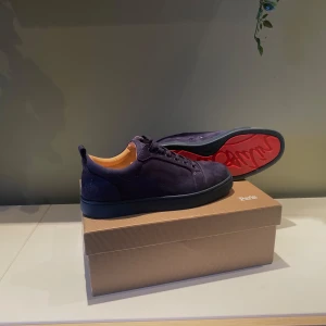 Mörkblå mocka sneakers från Louboutin - Snygga mörkblå sneakers från Christian Louboutin i lyxig mocka med ton-i-ton snörning och diskret broderad logga på hälen. Skorna har rund tå, platt sula och beige innersida i skinn. Perfekta för dig som gillar stilrena och exklusiva detaljer. Levereras med dustbag och handväska från Louboutin och box