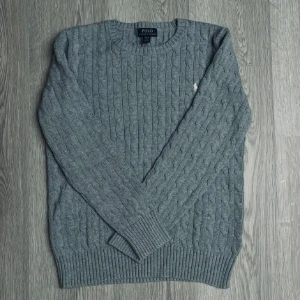 Grå kabelstickad tröja Polo Ralph Lauren - Säljer en klassisk grå kabelstickad tröja från Polo Ralph Lauren. Tröjan har rund halsringning och långa ärmar. Perfekt för lager-på-lager och enkel att matcha med olika outfits.                                         Storleken XL (18-20) motsvarar typ en storlek S.🙌🤝