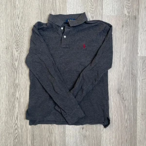 Mörkgrå pikétröja från Polo Ralph Lauren - Snygg mörkgrå långärmad pikétröja från Polo Ralph Lauren. Är i storlek 14-16 i barn vilket motsvarar en Xs-S🤝🙌