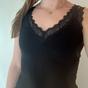 Svart linnetopp med spetskant - Snygg svart linnetopp med v-ringning och dekorativ spetskant längs halsringningen. Toppen är ärmlös och har en feminin och stilren look som passar perfekt till jeans eller kjol. Perfekt för dig som gillar enkla men ändå detaljerade plagg. Från Tezenis storlek S😊