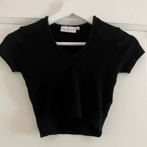 Svart croppad topp från Hennes - Svart croppad topp från Hennes Collection med v-ringning och korta ärmar. Toppens material är ribbat. Använd 3 gånger och i väldigt bra skick