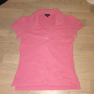 Rosa piké topp från Gant XS - Säljer en klassisk rosa piké topp från Gant i storlek XS. Toppen har korta ärmar, krage, knappar framtill och en liten bröstficka. Perfekt för dig som gillar en sportig och stilren look. Materialet är mjukt och skönt bomullstyg.