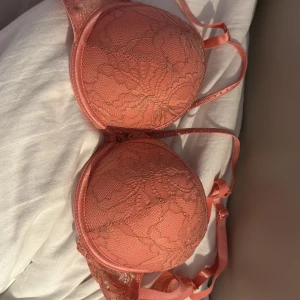 Korallrosa spets-bh från Censored - Superfin korallrosa bh från NyYorker  med spetsdetaljer och lätt vadderade kupor. Axelbanden är justerbara och bh:n har en snygg spetskant som ger en extra touch. Perfekt för dig som gillar färg och vill ha något lite extra i underklädeslådan. Storlek 75B men tänk på att den är i push-up. Provat en gång men den är tvättad 