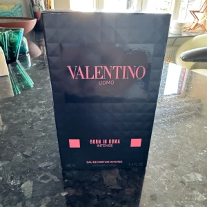 Valentino Uomo Born In Roma Intense 100ml - Valentino Uomo Born In Roma Intense Eau de Parfum i 100 ml flaska. Flaskan är lyxigt mönstrad i svart och transparent glas med rosa detaljer och svart kork med nitar. Doften är intensiv och modern, perfekt för dig som gillar exklusiva parfymer.