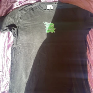 Svart t-shirt Vaillent XL med grön tryck - Svart t-shirt från Vaillent i storlek XL med coolt grönt tryck på bröstet och stor grafisk demon-illustration på ryggen. Texten 'Burn Baby Burn' och 'Demons Green Candy Sauce' ger en edgy vibe. Skön passform och klassisk rund hals.