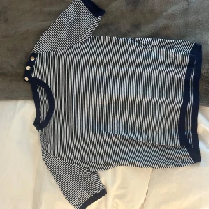 Randig kortärmad tröja med knappar - Snygg kortärmad tröja med marinblå och vita ränder. Tröjan har rund halsringning och tre guldiga knappar på axeln som cool detalj. Från Zara!! 