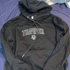 Svarta mjukisbyxor från Trapper - Svarta mjukisbyxor från Trapper med broderad logga på ena benet. Byxorna har snörning i midjan och dragkedjor på fickorna. Perfekta för chill eller träning, riktigt sköna och stilrena.