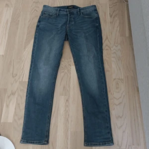 Blå jeans från Jack & Jones, 29/30 - Snygga blå jeans från Jack & Jones i klassisk tvätt. Modellen har raka ben och normal passform, med fem fickor och detaljerade sömmar. Perfekta för en avslappnad stil och funkar året runt. Materialet är slitstarkt jeans i bomull.