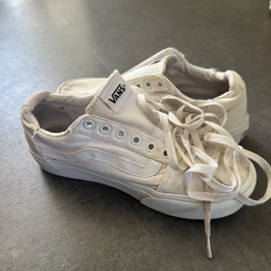 Vita Vans sneakers med platåsula - Säljer ett par klassiska vita Vans sneakers i canvas med platåsula och snörning. Skorna har rund tå och den ikoniska vågiga Vans-detaljen på sidan. Perfekta för dig som gillar en clean och stilren look med lite extra höjd.
