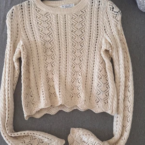 Beige stickad tröja från Amisu - Superfin beige stickad tröja från Amisu med snyggt hålmönster och långärmad modell. Tröjan har en croppad passform och rund halsringning, perfekt att styla med höga jeans eller kjol. Mjuk och skön, passar till flera säsonger.