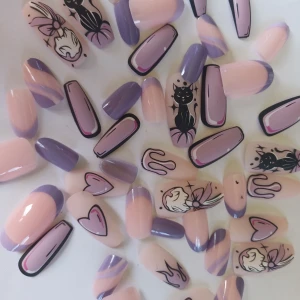 Lila och nude press-on naglar med motiv - Säljer ett set press-on naglar i nude och lila toner med coola motiv som katter, hjärtan, eld och grafiska linjer. Naglarna har både fransk tipp och helfärgade varianter, vissa med svart och rosa kontur. Perfekt för dig som vill ha unika och trendiga naglar.
